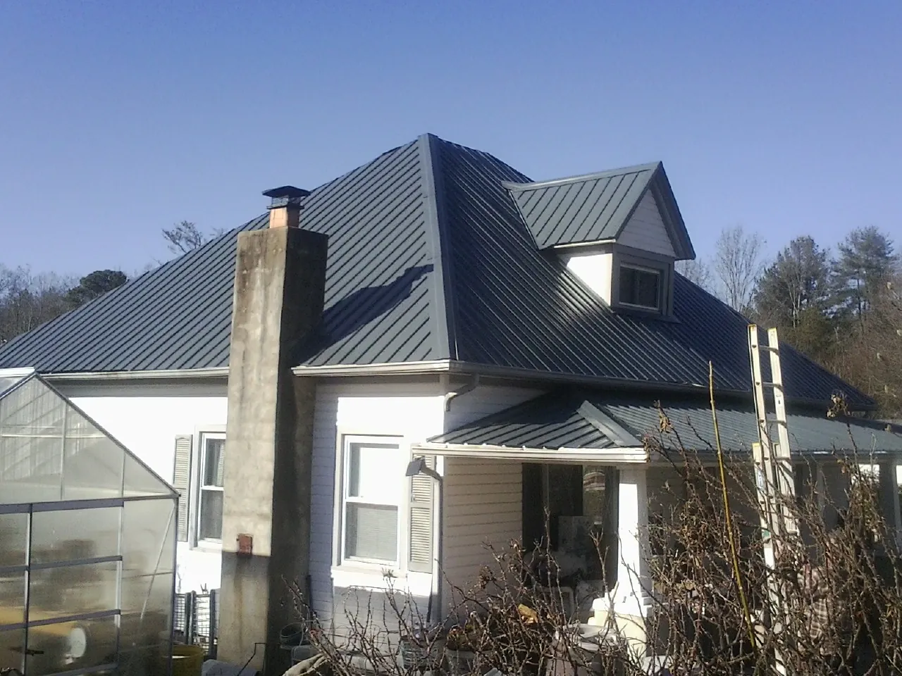 Dark blue standing seam metal roof on a white farmhouse with dormer — Slate & Tile Roof Repair by Roofing Brothers in Titusville
