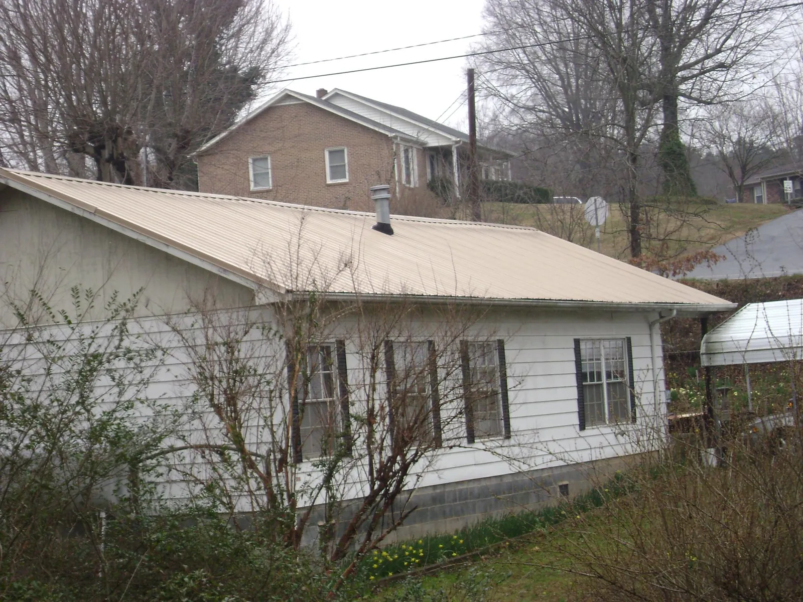 Tan metal roof on a white sided house set into a hillside — Commercial Roofing by Roofing Brothers in Titusville